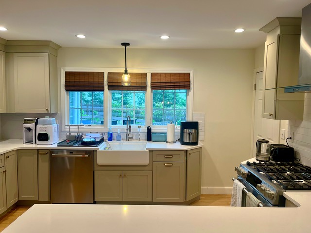 Clean residential kitchen cleaned by Sandy Cares, with sage-green cabinets, a farmhouse sink, and clear countertops.